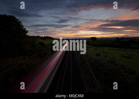 La vitesse des trains Pendolino Virgin Trains vers le coucher du soleil sur la ligne principale de la côte ouest dans la région de Cumbria. Banque D'Images
