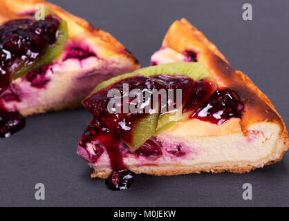 Un morceau de gâteau de fromage blanc aux cerises est coulé avec de la confiture sur une surface noire Banque D'Images