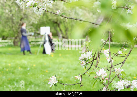 Girl peintures peinture sur toile de chevalet dans parc avec sakura en fleurs. Image floue pour le printemps creative background Banque D'Images