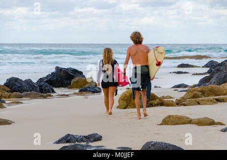 Surfers mâles et femelles à pied à travers l'océan plage vers l'exécution des planches Banque D'Images