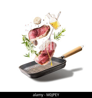 Steaks de boeuf cru de vol, avec des herbes, l'huile et des épices avec poêle et des ustensiles de cuisine, isolé sur fond blanc, de face. Flying food concept Banque D'Images