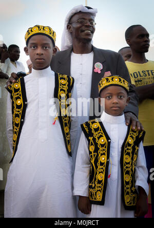 Les enfants portant costume traditionnel pour le Mawlid kufi & festival, fête avec leur père dans l'île de Lamu corniche bondé, au Kenya Banque D'Images