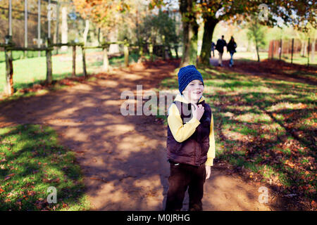 Un petit garçon souriant, vêci de vêtements chauds, est prêt à s'amuser dans un parc d'automne doré au Royaume-Uni. Lumière d'automne, liberté, bonheur, enfance. Banque D'Images