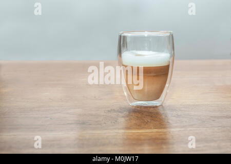 Une vitre avec un latte machiato sur une table en bois Banque D'Images