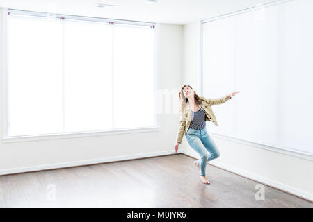 Une jeune femme souriante heureuse sauter de haut vide dans la nouvelle chambre moderne avec du parquet et de grandes fenêtres ensoleillées dans l'appartement Banque D'Images