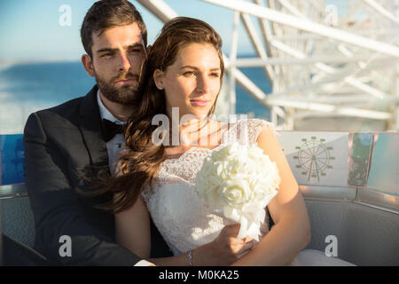 Jeunes mariés posent pour après le mariage portrait équestre grande roue près de ocean Banque D'Images