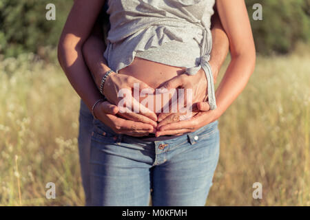 Couple en attente d'un enfant et s'étreindre les uns les autres avec leurs mains sur baby bump. Banque D'Images