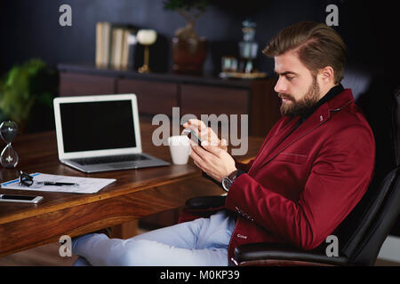 Un homme d'utiliser son mobilephone at home office Banque D'Images