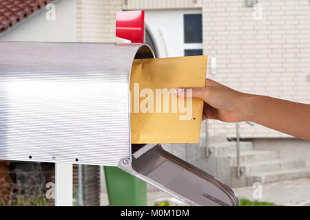 Close-up of a person's Hand dépose une lettre de la boîte aux lettres d'argent Banque D'Images
