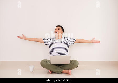 Jeune homme jouant sur laptop sitting on floor appréciant gagner ou de bonnes nouvelles Banque D'Images