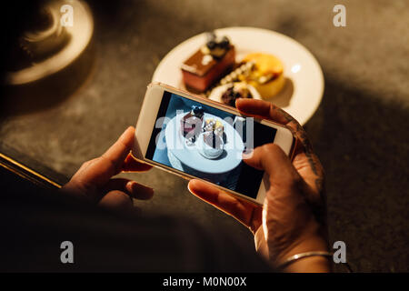 Femme utilise son téléphone pour prendre une photo d'un plateau de thé de l'après-midi. Banque D'Images