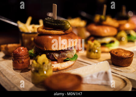 Gros plan d'un burger restaurant repas avec des oignons, du bacon, le cornichon, plaquettes et garnitures. Banque D'Images