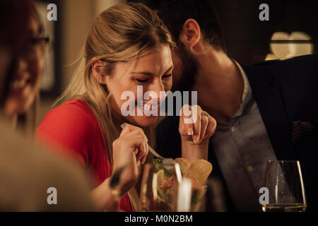 Couple romantique sont en cours tout en ayant un repas dans un restaurant. L'homme embrasse la femme sur sur la joue et elle est en riant. Banque D'Images