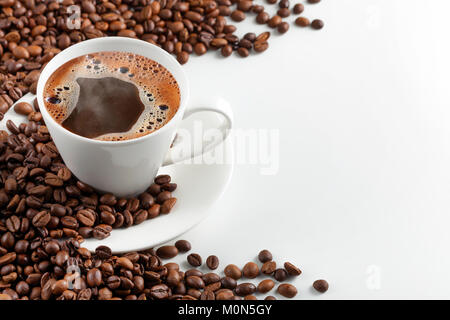 Une tasse de café chaud avec de la mousse dans un éparpillement de grains de café sur fond blanc Banque D'Images