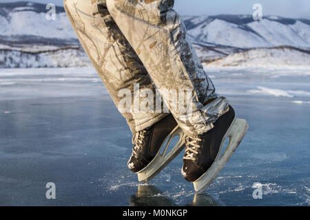 Un patineur homme en noir patins en hiver au chaud pantalon de ski montre un moon walk sur la glace bleue claire du sacré Lac Baikal en hiver. Banque D'Images