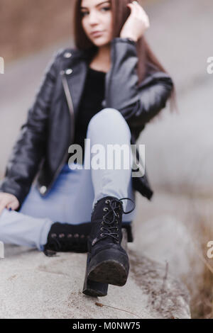 Jeune femme portant des bottines noires à talons hauts, assis sur une roche en plein air avec l'accent pour le boot Banque D'Images