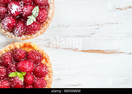 Tartelettes à la framboise avec des feuilles de menthe et couverts de sucre glace sur fond blanc Banque D'Images