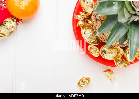 Le nouvel an chinois ang pow concept.Vue de dessus de l'ananas avec groupe de lingots d'or dans le bac rouge sur table en bois blanc.sur moyenne des lingots riches. Banque D'Images