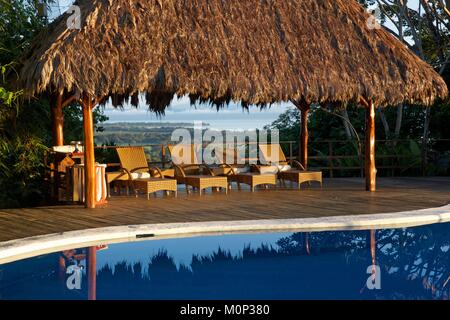 Costa Rica, Osa peninsula,transats alignés au bord de la piscine de l'ecolodge Lapa Rios sous un pavillon avec toit vert,donnant sur l'océan Banque D'Images