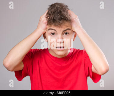 Portrait psychologique de teen boy. Funny cute surpris enfant jeune de 14 ans avec la bouche ouverte dans l'étonnement. Adolescent choqué avec les mains sur la tête, sur la g Banque D'Images