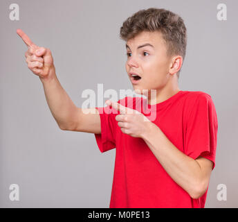 Portrait psychologique de teen boy. Funny cute surpris enfant jeune de 14 ans avec la bouche ouverte dans l'étonnement. Adolescent choqué pointer du doigt vers le haut, sur Banque D'Images