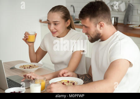 Jeune couple prendre le petit-déjeuner à parler à l'aide de l'ordinateur portable sur coin t Banque D'Images