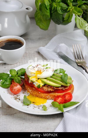 Œuf poché sur une tranche de baguette grillée avec tomates, jambon épicé et d'avocat, saupoudré d'épices et de basilic. Banque D'Images