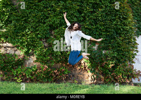 Happy girl jumping millénaire librement contre le mur du jardin en été. Banque D'Images