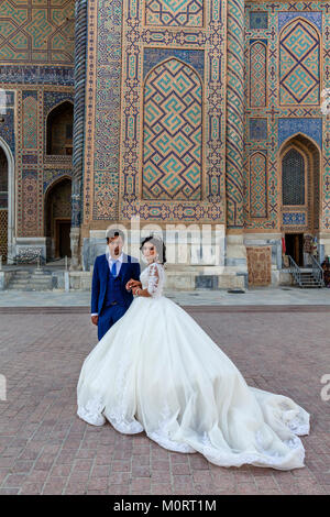 Un 'juste' jeune couple mariés posent pour une photo au complexe du Registan, Samarkand, Ouzbékistan Banque D'Images