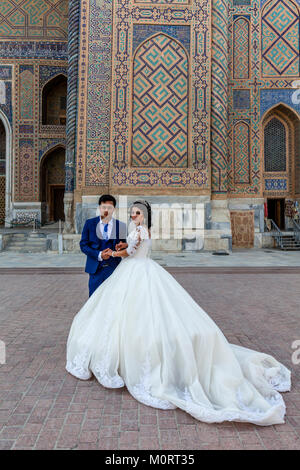 Un 'juste' jeune couple mariés posent pour une photo au complexe du Registan, Samarkand, Ouzbékistan Banque D'Images