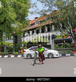 Un vieux javanais femme entre son vélo de l'autre côté de la rue. Semarang, Java, Indonésie. La construction de chemins de fer est dans l'arrière-plan. Banque D'Images