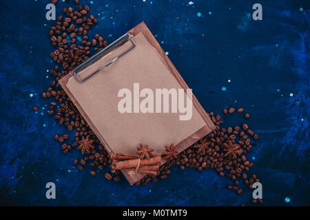 Presse-papiers en bois blanc avec du papier craft dans un en-tête avec des grains de café et d'épices. Ingrédients pour faire du café dans un concept créatif mise à plat. Banque D'Images