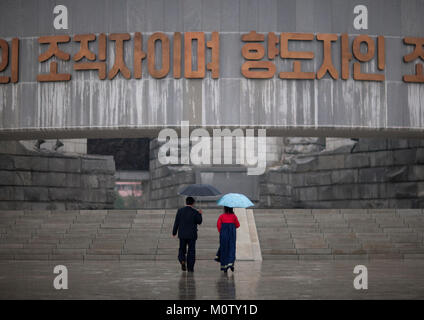 L'homme et de la femme en Corée du Nord sous un parapluie aller au monument de parti, de la province de Pyongan, Pyongyang, Corée du Nord Banque D'Images