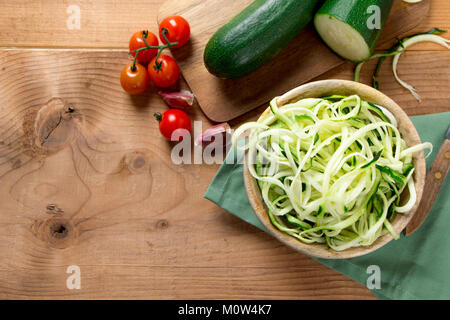 Les nouilles brutes avec courgettes Tomates cerises dans un bol en bois sur une table en bois rustique. Vue d'en haut Banque D'Images