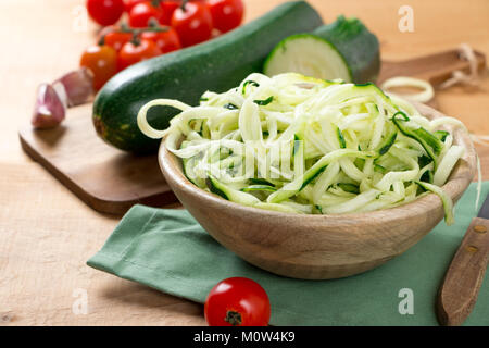 Les nouilles brutes avec courgettes Tomates cerises dans un bol en bois sur une table en bois rustique. Banque D'Images