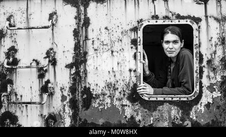 Portrait d'une jeune femme dans la fenêtre d'un objet rouillé fer abandonnée. Photo en noir et blanc. Banque D'Images