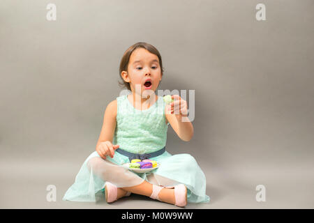 Petite fille excité avec une assiette pleine de macarons Banque D'Images