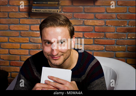 Studio portrait of man with book assis sur une chaise contre avec cloche de décorations. Banque D'Images