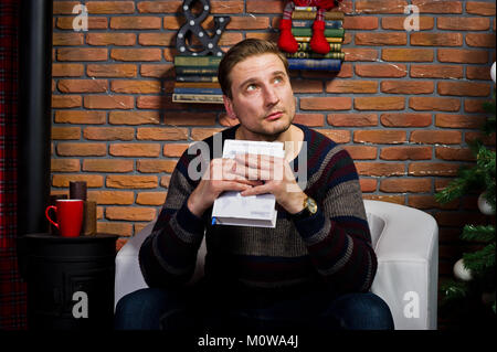 Studio portrait of man with book assis sur une chaise contre avec cloche de décorations. Banque D'Images