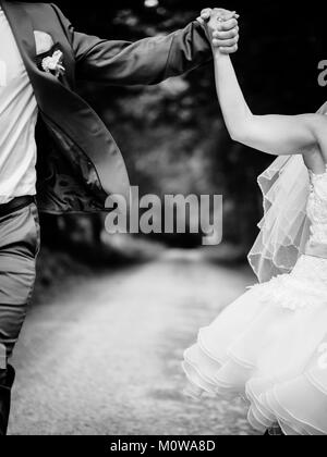 Saut à la mariée et le marié, se tenant la main et sauter, est très heureux, noir et blanc Banque D'Images