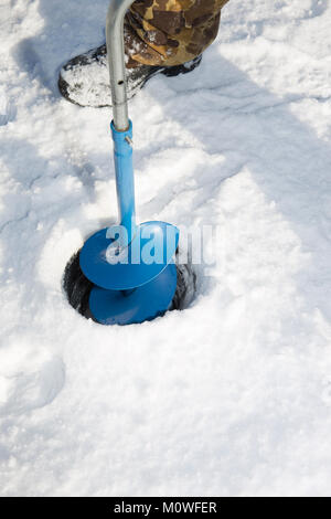 Une personne de percer un trou dans la glace d'un lac gelé à l'aide d'une glace auguer (une vis hélicoïdale à lames). Banque D'Images