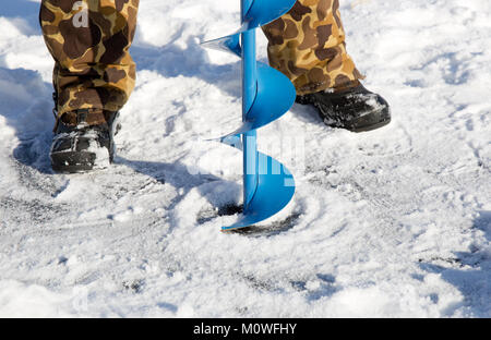 Une personne de percer un trou dans la glace d'un lac gelé à l'aide d'une glace auguer (une vis hélicoïdale à lames). Banque D'Images