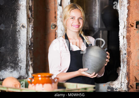 Portrait of smiling young woman holding potter en céramique émaillée noire à côté du navire Four Banque D'Images