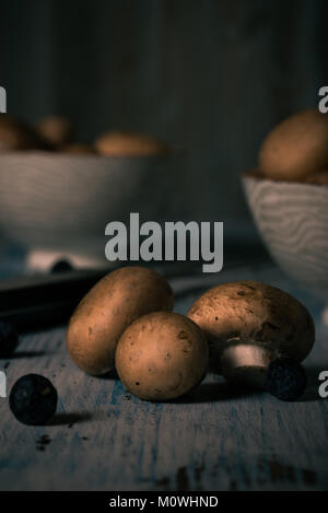 Photo verticale de plusieurs champignons comestibles avec brown vintage caps sur planche de bois. Champignons est renversé sur table avec la couleur bleu usé. Céramique 2 Banque D'Images