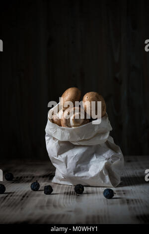 Photo verticale de plusieurs champignons comestibles brun. Champignons sont placés dans des sacs en papier blanc sur blanc en bois avec bureau vintage couleur usés. Plusieurs bla Banque D'Images