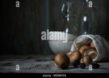 Photo horizontale de plusieurs champignons comestibles brun. Champignons est renversé sur planche de bois blanc à partir de sac de papier. Quelques backthorn sont de petits fruits bleu foncé Banque D'Images