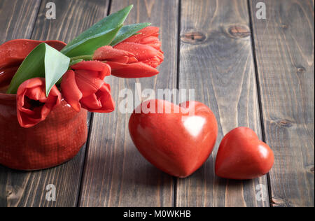 Deux coeurs de pierre et bouquet de tulipes rouges sur fond de bois. Conception de carte de vœux pour la Saint-Valentin, fête des mères ou des pères. Banque D'Images