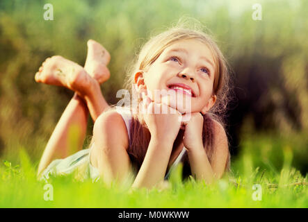Joyeux Heureux petite fille à l'école élémentaire âge allongé sur l'herbe verte dans le parc Banque D'Images