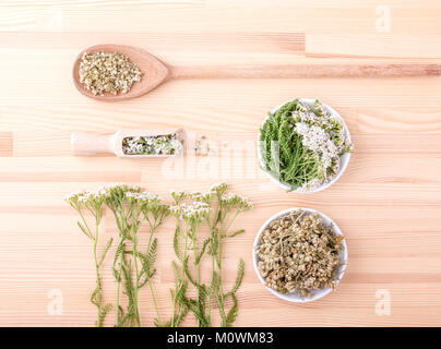 Vue de dessus deux cuillères de beurre frais et de fleurs séchées et des feuilles d'achillée avec un fond de bois Banque D'Images