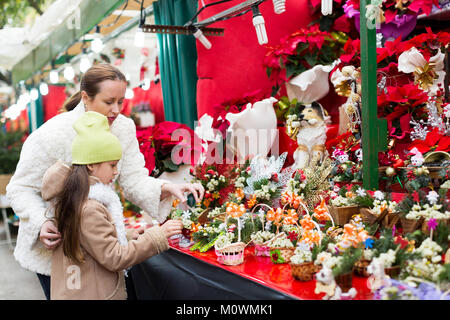 Femme heureuse avec sa petite fille l'achat composition florale de Noël avec le gui en marché. Se concentrer sur la fille Banque D'Images